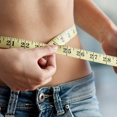 A woman using a tape measure to measure her waist